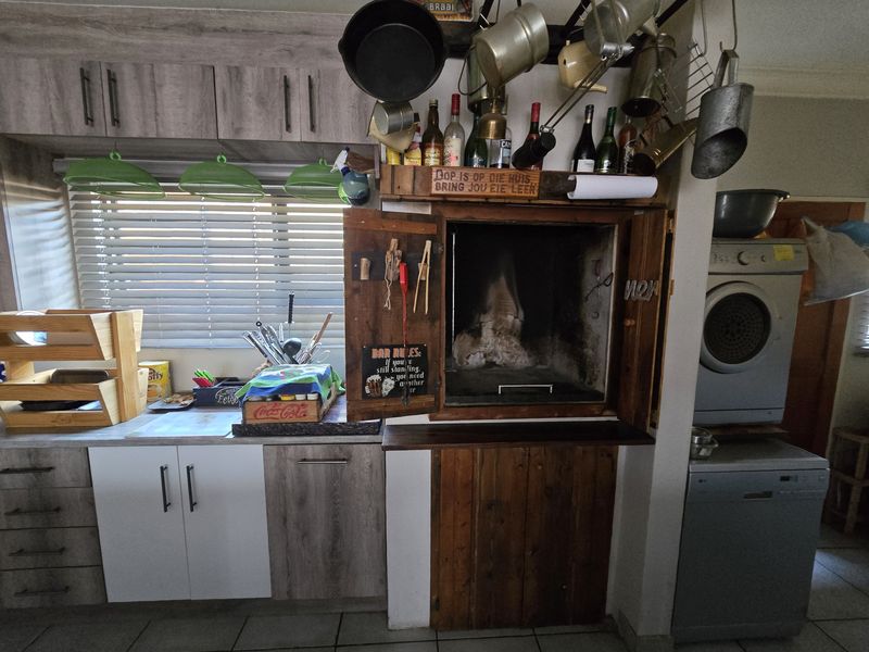 Kitchen area featuring a built-in indoor braai, wood-look cabinetry, tiled flooring, and integrated space for laundry appliances.