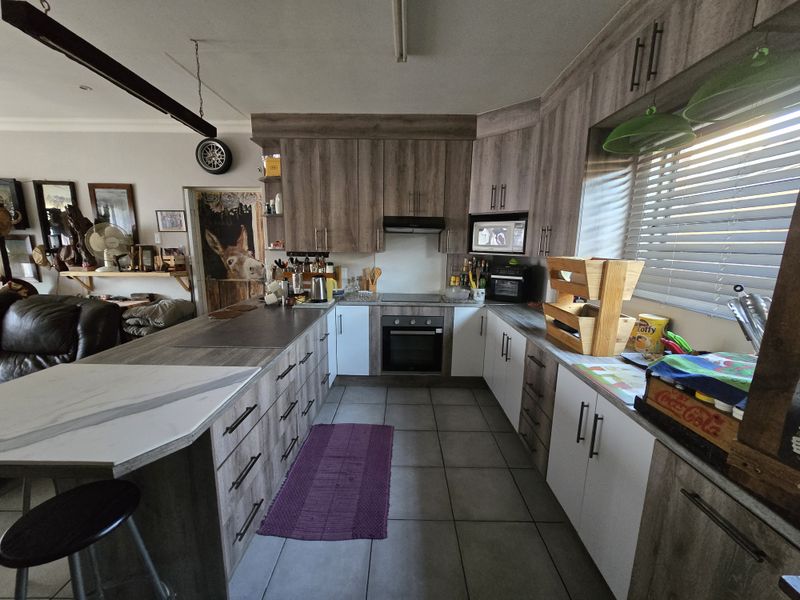 Modern kitchen featuring wood-grain cabinetry, a central island, built-in oven and hob, and tiled flooring, offering a functional and contemporary workspace.