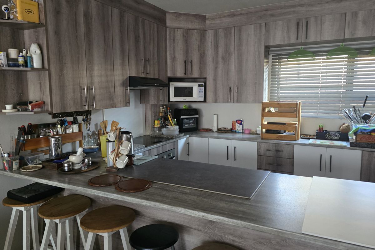Modern kitchen featuring wood-look laminate cabinetry, a breakfast bar, built-in microwave, and extractor fan with natural light from the window.
