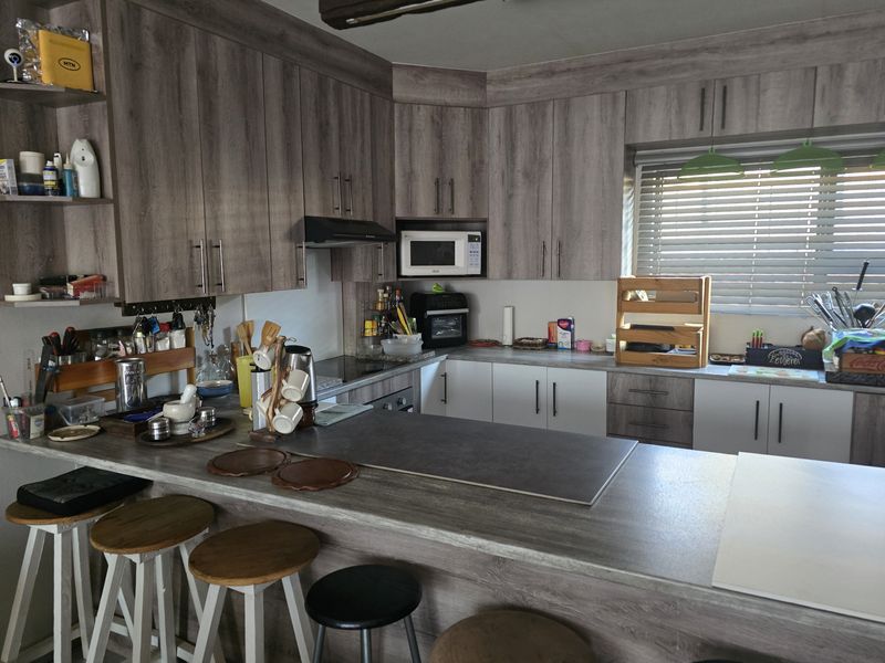 Modern kitchen featuring wood-look laminate cabinetry, a breakfast bar, built-in microwave, and extractor fan with natural light from the window.
