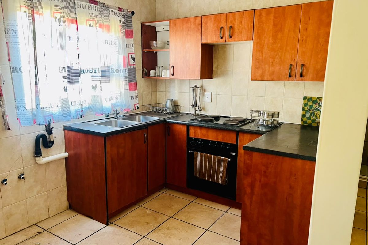 A functional kitchen featuring wood-look cabinetry, dark laminate countertops, built-in oven, electric hob, and tiled finishes throughout.