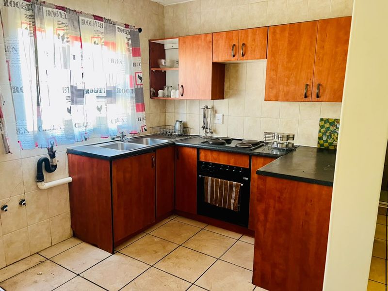 A functional kitchen featuring wood-look cabinetry, dark laminate countertops, built-in oven, electric hob, and tiled finishes throughout.