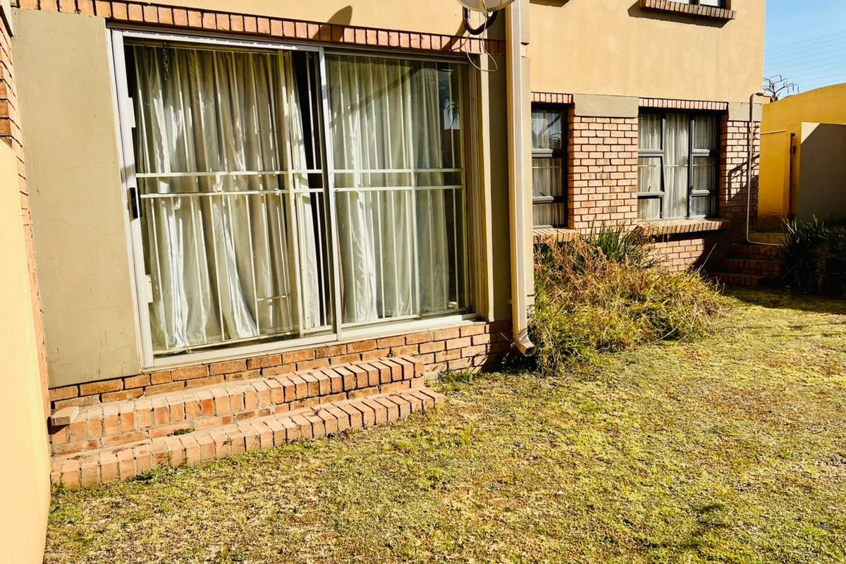 Rear view of the apartment featuring a sliding glass door, brick exterior facade, and a small garden area.