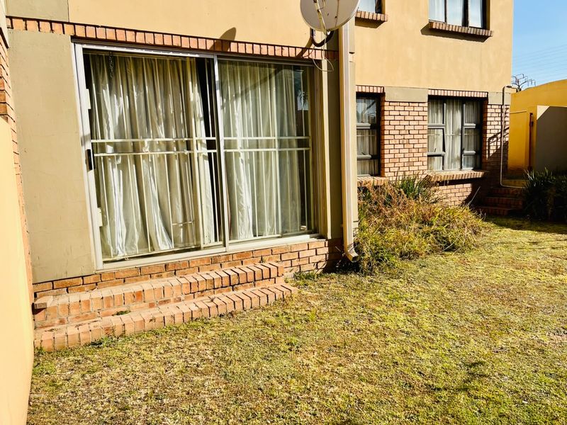 Rear view of the apartment featuring a sliding glass door, brick exterior facade, and a small garden area.