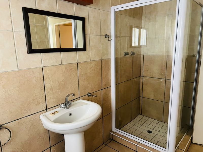 A functional bathroom featuring a pedestal basin, tiled walls, and a separate shower enclosure with a white frame.