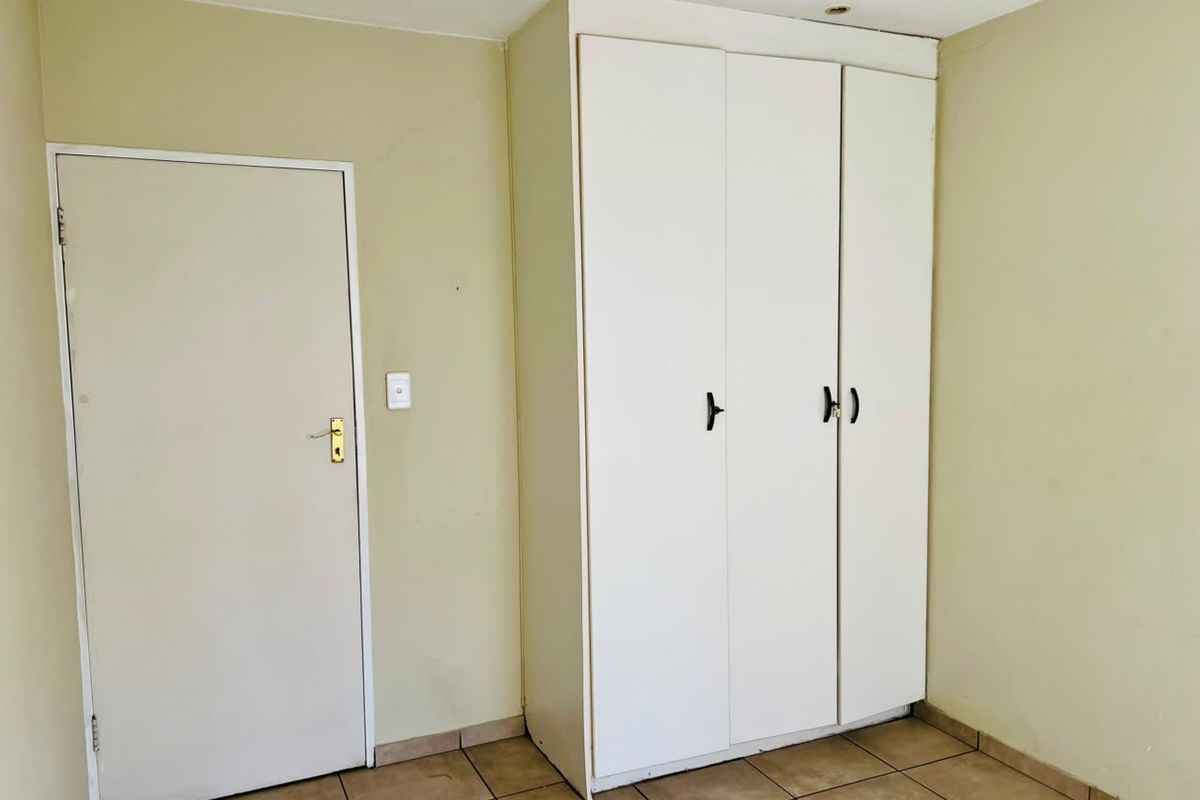 A simple bedroom featuring neutral walls, tiled flooring, and a functional built-in wardrobe with white cabinetry.
