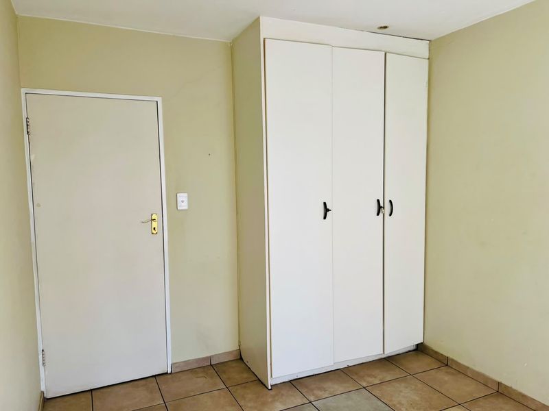 A simple bedroom featuring neutral walls, tiled flooring, and a functional built-in wardrobe with white cabinetry.