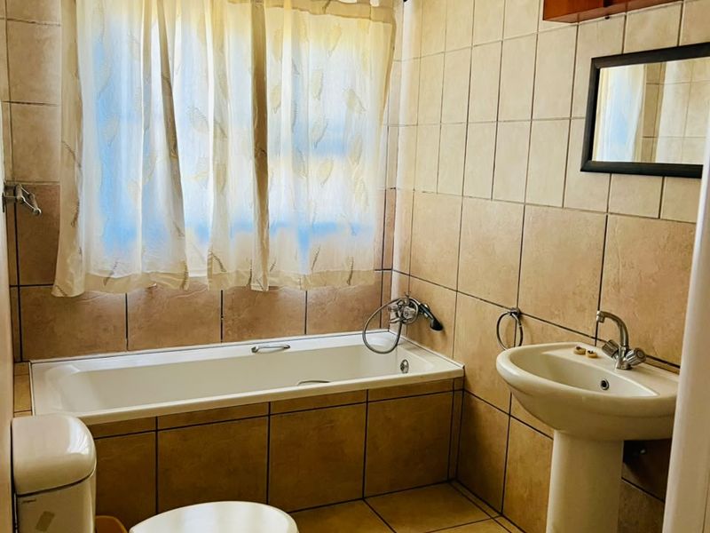 A functional bathroom featuring a bathtub, pedestal basin, and toilet with neutral wall and floor tiling.