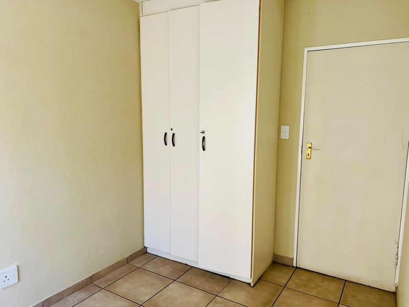A simple bedroom featuring tiled flooring and a built-in white wardrobe with standard internal door access.