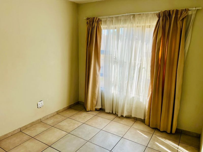 An empty bedroom featuring neutral tiled flooring and a large window with installed curtain rods, providing a blank canvas for personalization.