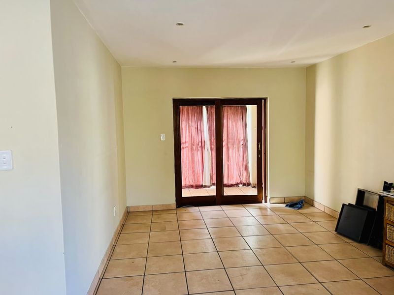 An empty living room featuring tiled flooring, recessed downlights, and a sliding glass door providing access to the exterior.