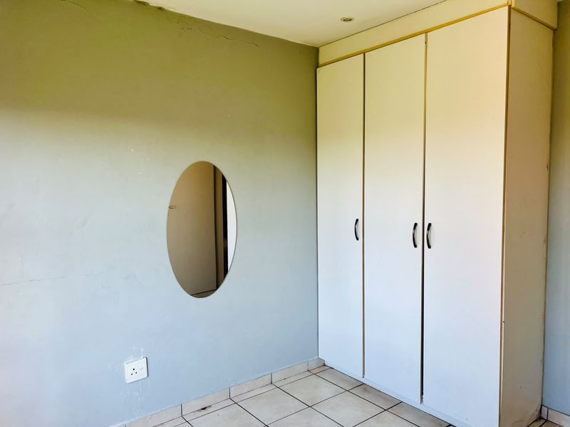 A vacant bedroom featuring built-in wardrobes, tiled flooring, and visible wall imperfections, offering a blank canvas for potential renovation or interior design updates.