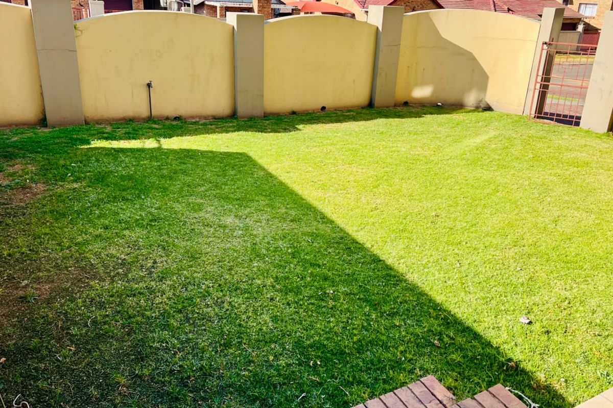 A private rear garden area featuring a well-maintained lawn, enclosed by high boundary walls and a secure metal gate.