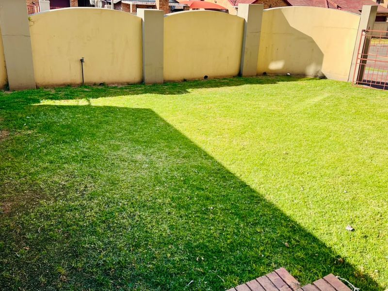 A private rear garden area featuring a well-maintained lawn, enclosed by high boundary walls and a secure metal gate.