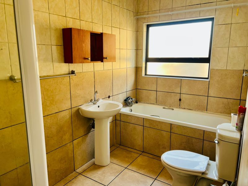 A functional bathroom featuring a pedestal basin, bathtub, toilet, and wall-mounted storage cabinet, finished with neutral wall and floor tiling.