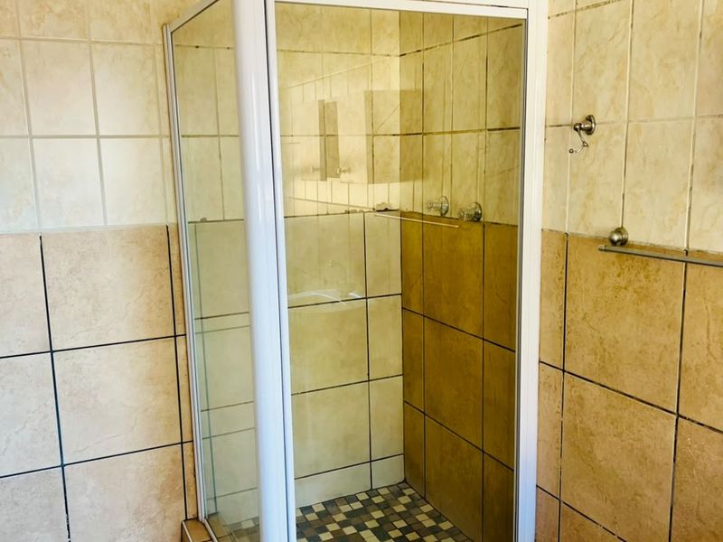 A functional bathroom featuring a corner shower enclosure with tiled walls and flooring, requiring some maintenance and cosmetic updates.