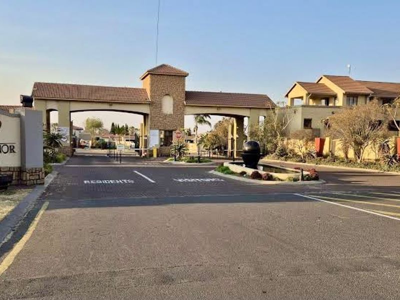 The main entrance and security gatehouse of the Revo Manor apartment complex, featuring paved access roads and a decorative water feature.