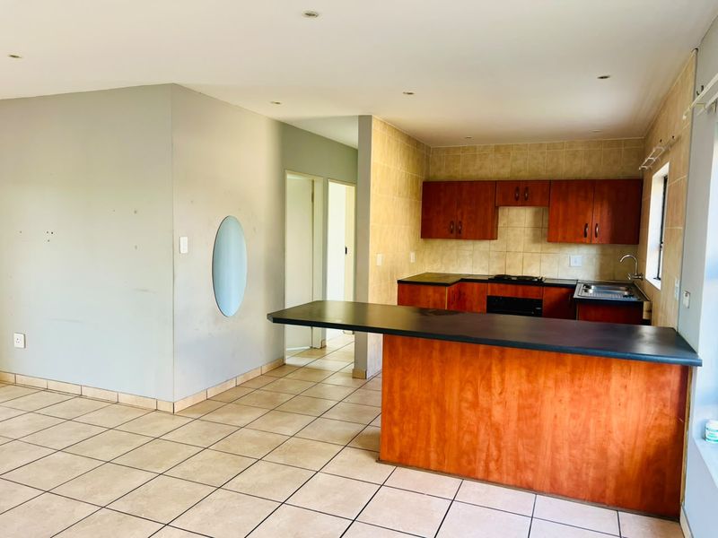 Open-plan kitchen and living area featuring wooden cabinetry, a breakfast bar, tiled flooring, and recessed lighting in a neutral, functional layout.