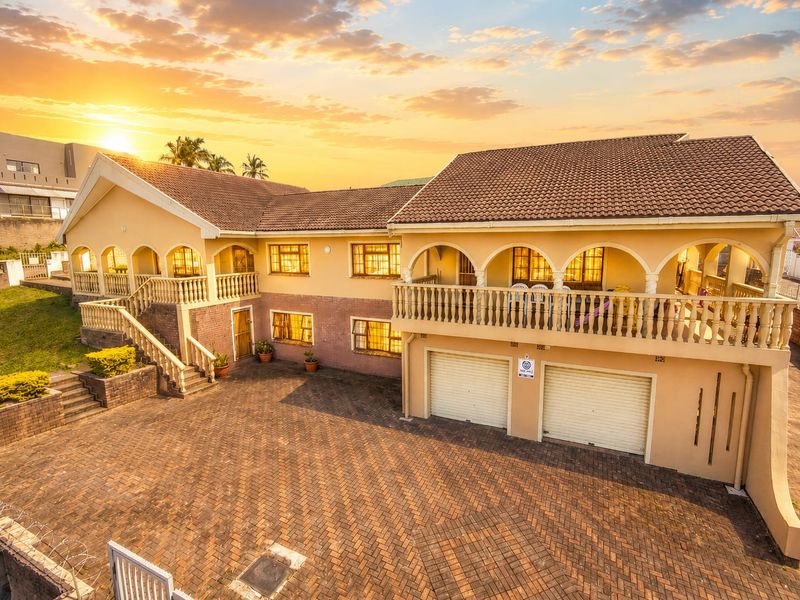 A spacious multi-level residential property featuring a paved driveway, double garage, and an expansive upper-level arched veranda with classic balustrade detailing.