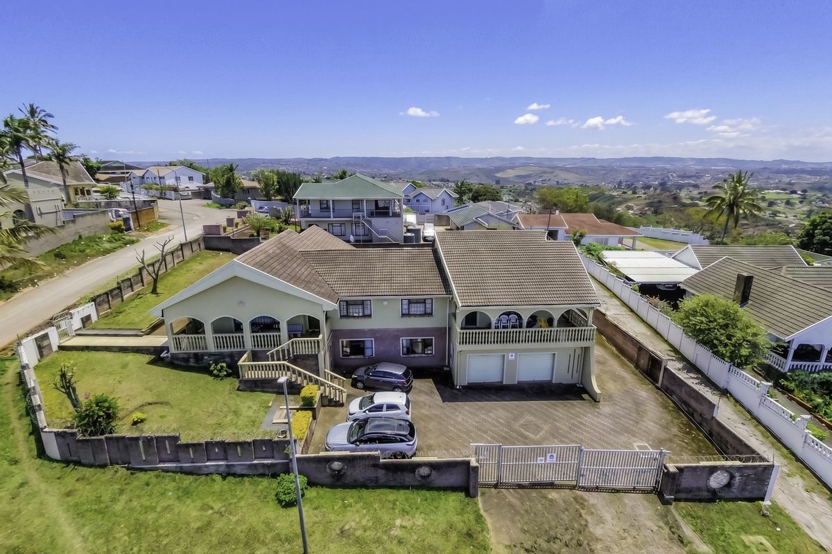 Aerial view of a multi-level residential property featuring a tiled roof, double garage, paved driveway, and perimeter wall with security gate.