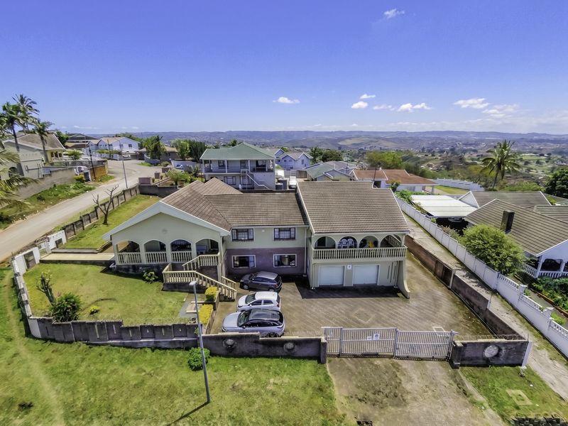 Aerial view of a multi-level residential property featuring a tiled roof, double garage, paved driveway, and perimeter wall with security gate.