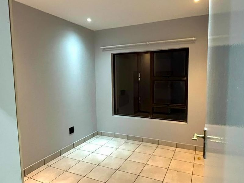 A clean, empty bedroom featuring neutral grey walls, tiled flooring, and recessed downlighting, providing a versatile space ready for personalization.