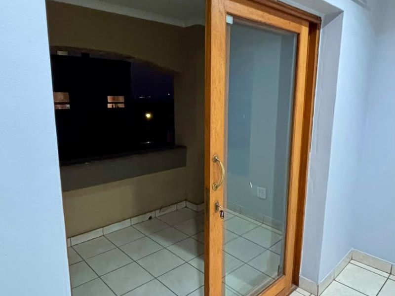 A tiled balcony area accessed through a wooden sliding glass door, featuring neutral wall tones and functional curtain tracks.