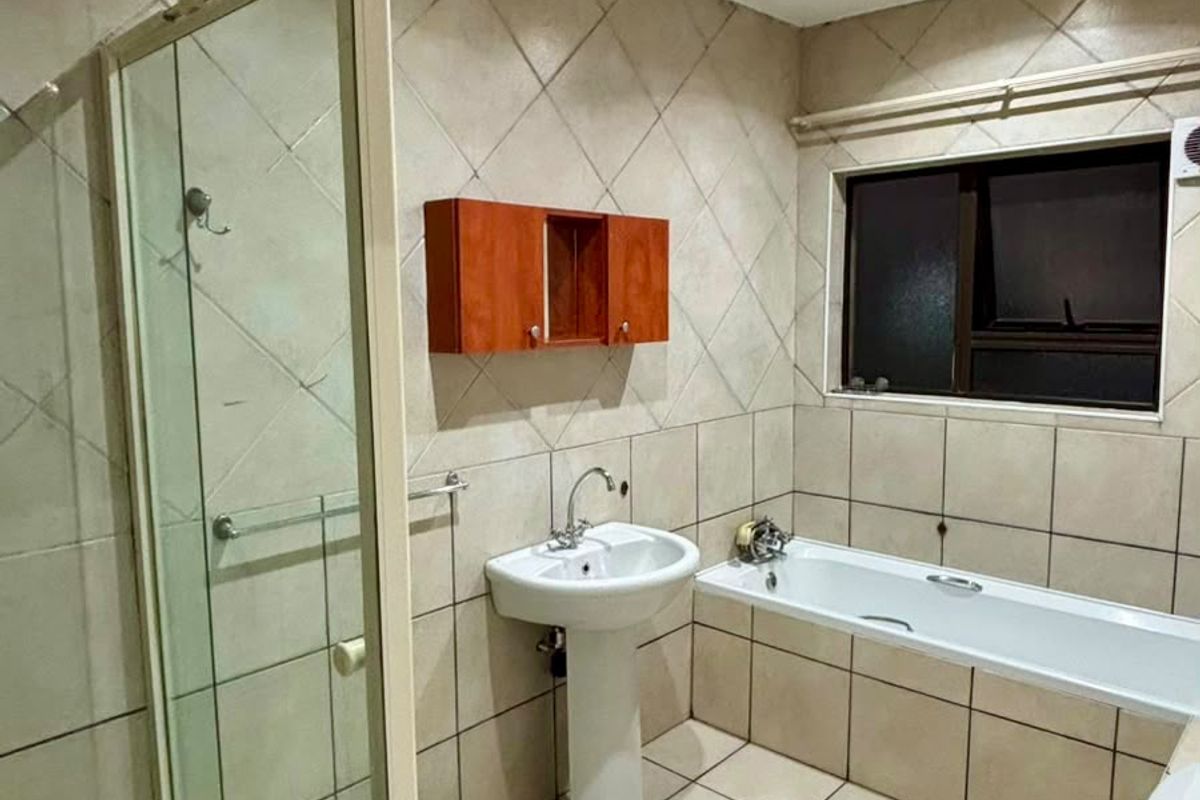 A functional bathroom featuring a separate shower enclosure, bathtub, pedestal basin, and toilet with neutral tiled finishes throughout.