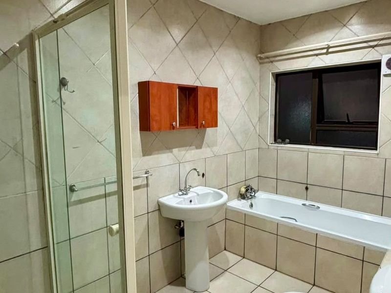 A functional bathroom featuring a separate shower enclosure, bathtub, pedestal basin, and toilet with neutral tiled finishes throughout.