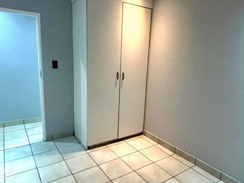 A clean, empty bedroom featuring neutral tiled flooring, light grey walls, and a built-in wardrobe with integrated lighting.