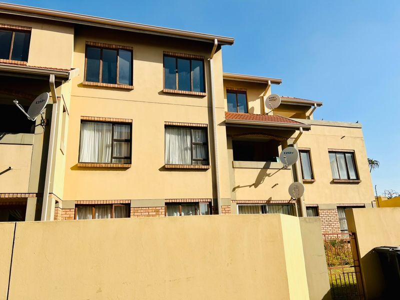 A multi-story apartment building facade featuring a warm-toned exterior, tiled roof, and multiple balconies with satellite dish installations.