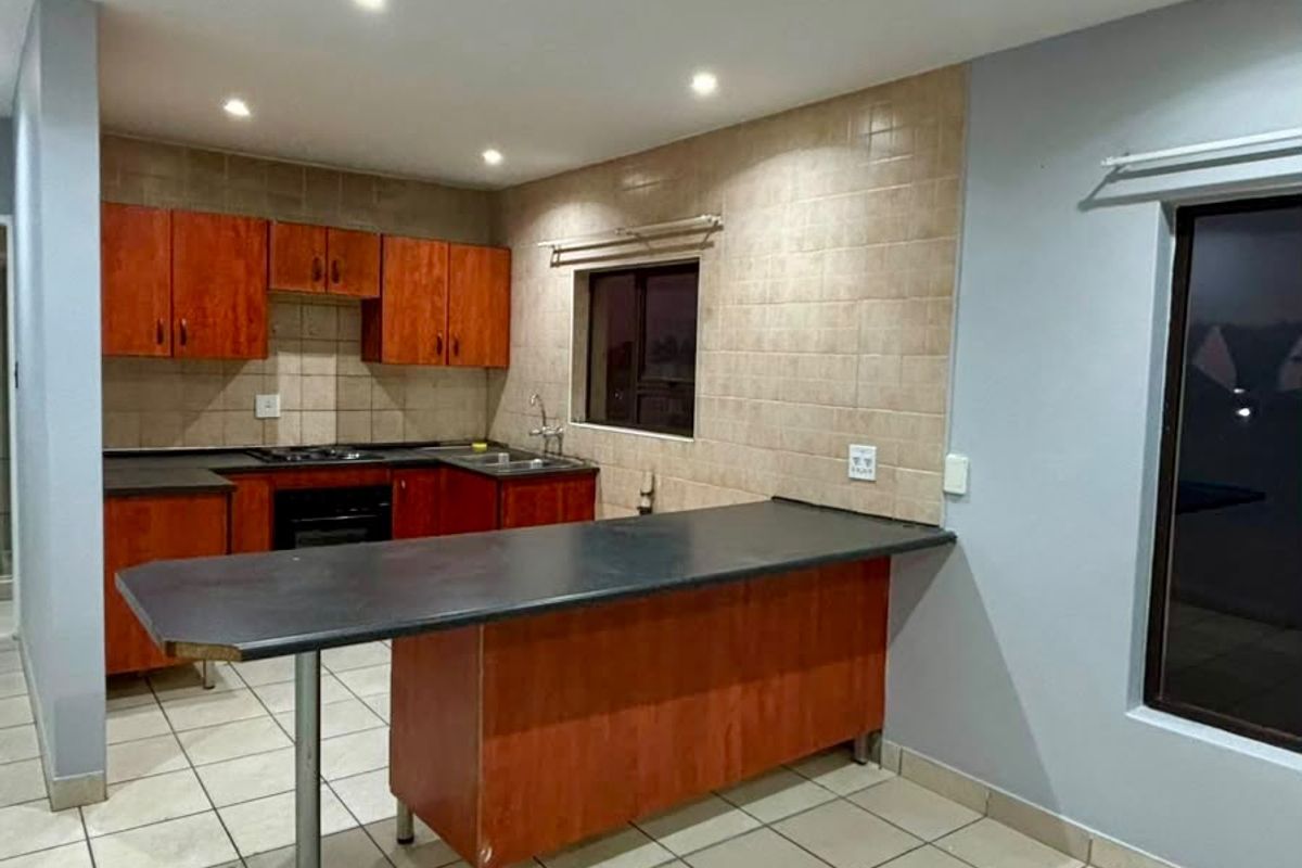 A functional kitchen featuring wooden cabinetry, a breakfast bar, tiled backsplash, and integrated appliances, offering a clean and practical layout.