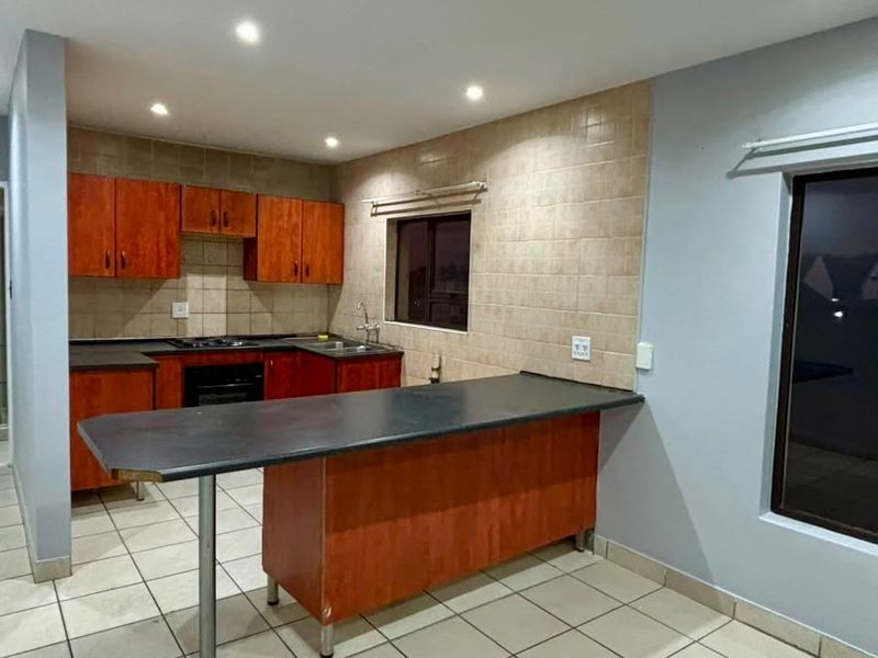 A functional kitchen featuring wooden cabinetry, a breakfast bar, tiled backsplash, and integrated appliances, offering a clean and practical layout.