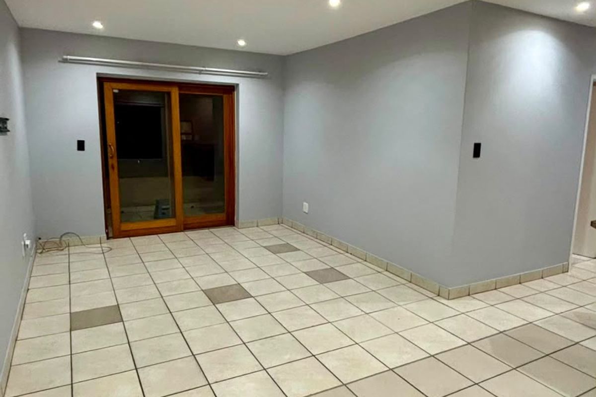 An empty living area featuring neutral grey walls, ceramic tiled flooring with accent tiles, and a sliding glass door providing access to the exterior.