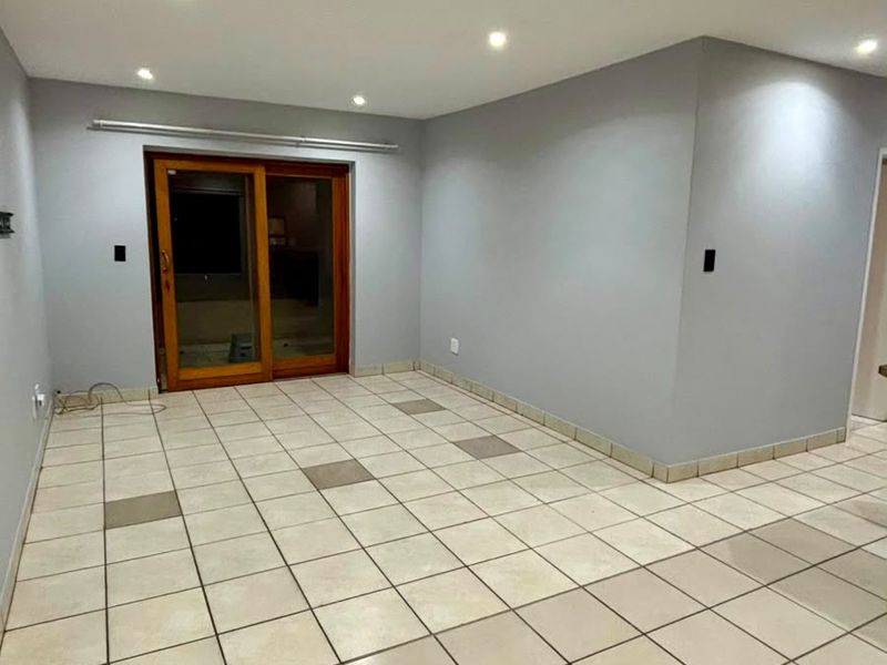 An empty living area featuring neutral grey walls, ceramic tiled flooring with accent tiles, and a sliding glass door providing access to the exterior.