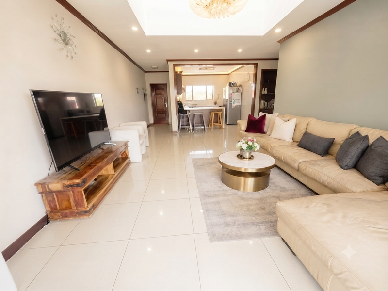Spacious open-plan living area featuring polished floor tiles, a recessed ceiling with integrated lighting, and a seamless transition to the kitchen and breakfast bar.