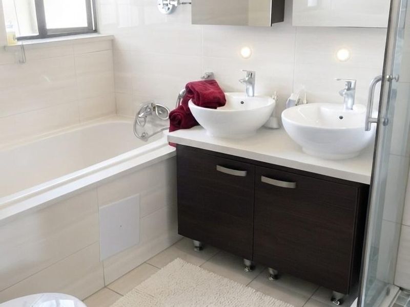 Modern bathroom featuring a double vanity with vessel sinks, a built-in bathtub, and a separate glass-enclosed shower with neutral wall and floor tiling.