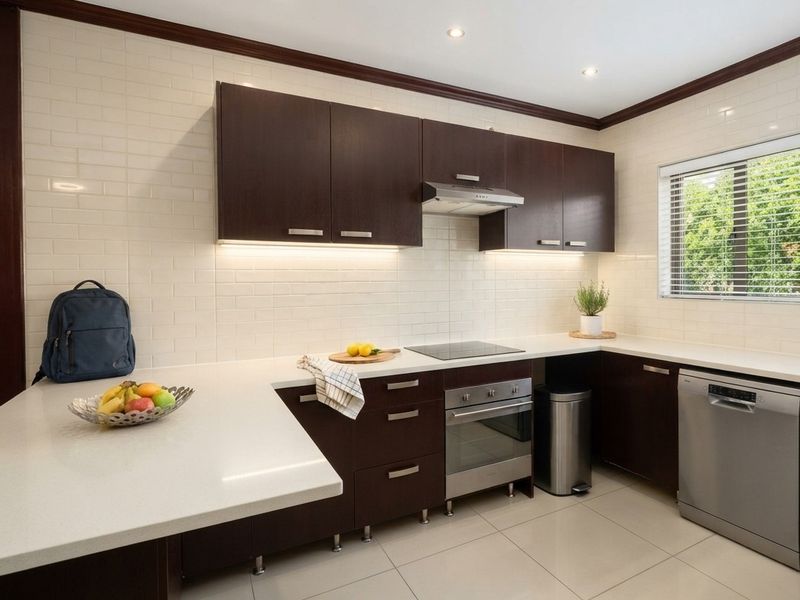 Modern kitchen featuring dark wood cabinetry, white stone countertops, subway tile backsplash, and integrated appliances including an electric cooktop and oven.