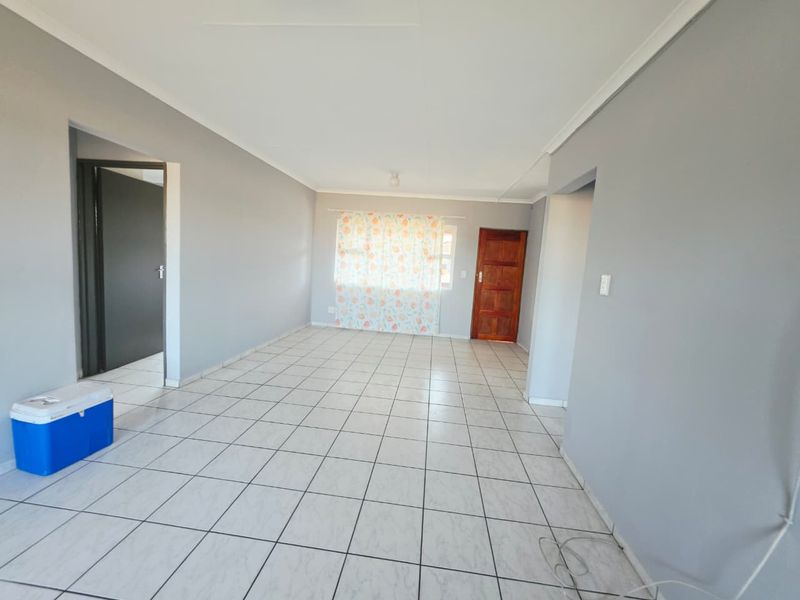 A spacious, empty living area featuring neutral grey walls, white tiled flooring, and a wooden door, offering a blank canvas for interior design.