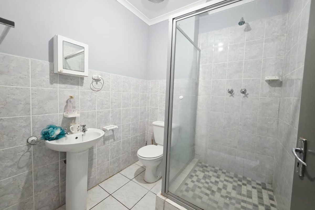 A functional bathroom featuring a pedestal basin, a glass-enclosed shower, and tiled finishes throughout.