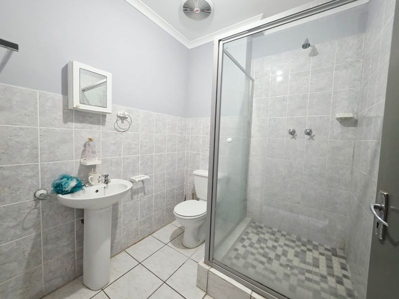 A functional bathroom featuring a pedestal basin, a glass-enclosed shower, and tiled finishes throughout.