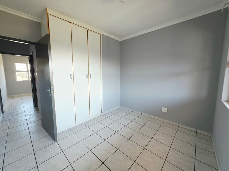 A clean, empty bedroom featuring neutral grey walls, white built-in cupboards, and tiled flooring, offering a versatile space ready for personalization.