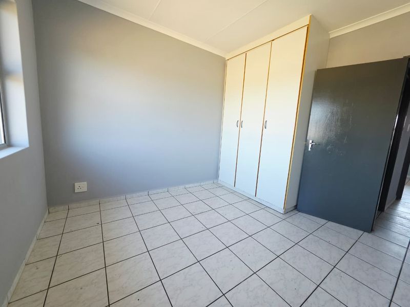 A clean, empty bedroom featuring neutral grey walls, white tiled flooring, and a built-in wardrobe with white doors.