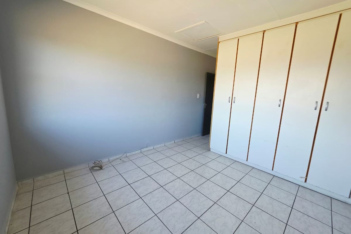 A bright, empty bedroom featuring neutral grey walls, white tiled flooring, and ample built-in cupboard storage.