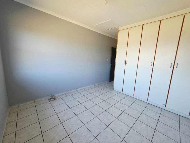 A bright, empty bedroom featuring neutral grey walls, white tiled flooring, and ample built-in cupboard storage.