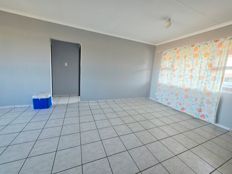 A bright, empty living room featuring neutral grey walls and clean ceramic floor tiles, offering a versatile blank canvas for interior design.