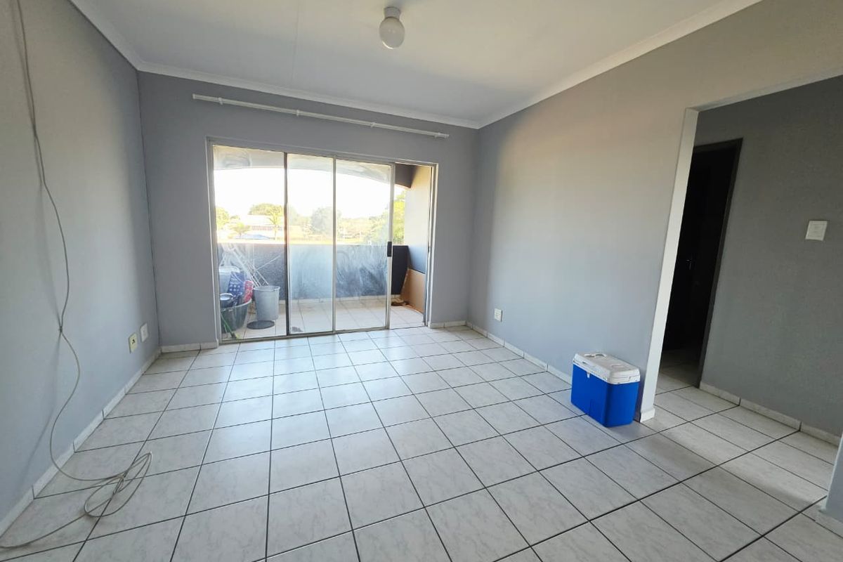 An empty living room featuring neutral grey walls, ceramic tiled flooring, and a large sliding glass door providing access to an outdoor balcony area.
