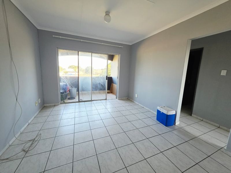An empty living room featuring neutral grey walls, ceramic tiled flooring, and a large sliding glass door providing access to an outdoor balcony area.