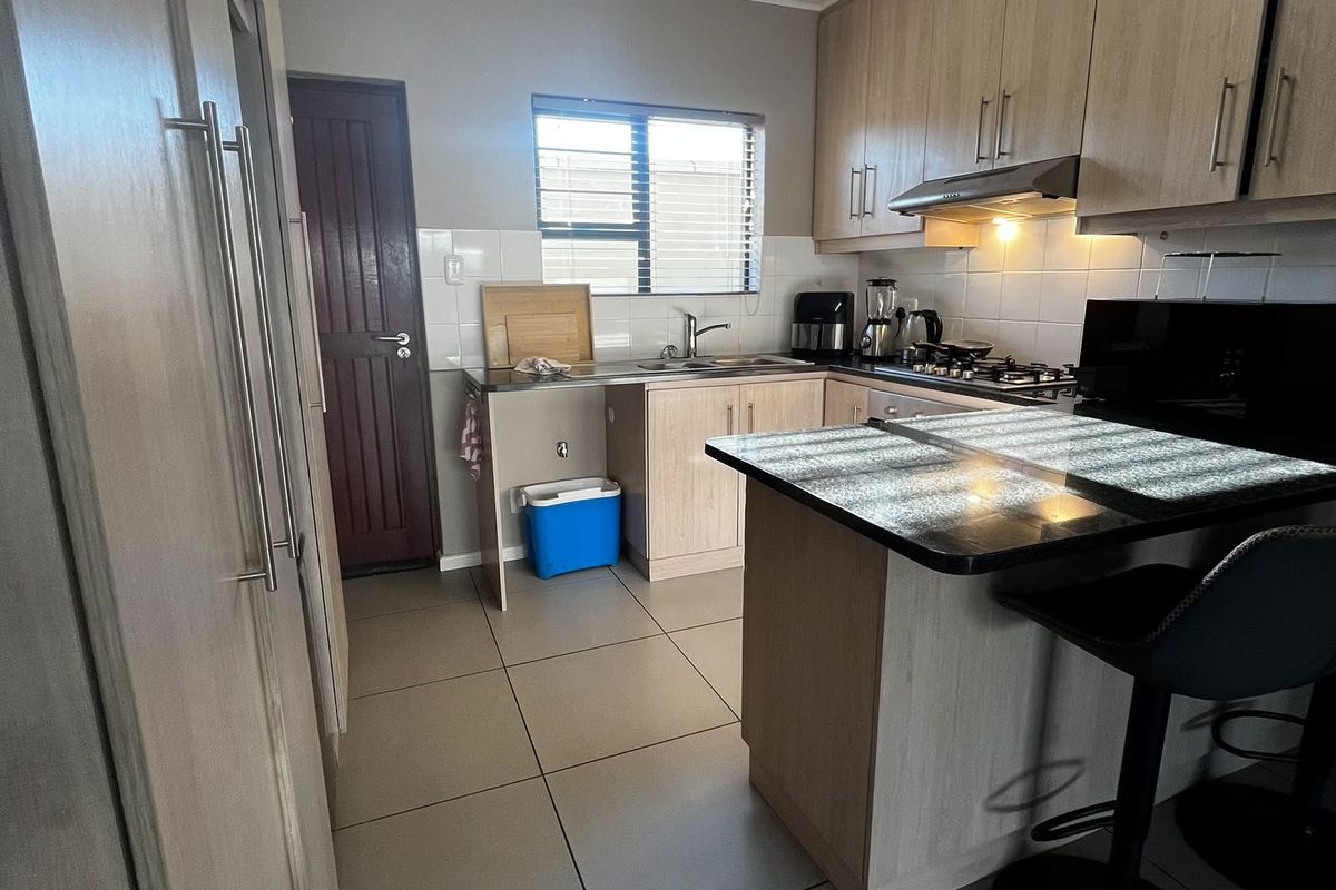 A functional kitchen featuring light wood cabinetry, dark countertops, a breakfast bar, gas hob with extractor, and tiled flooring.