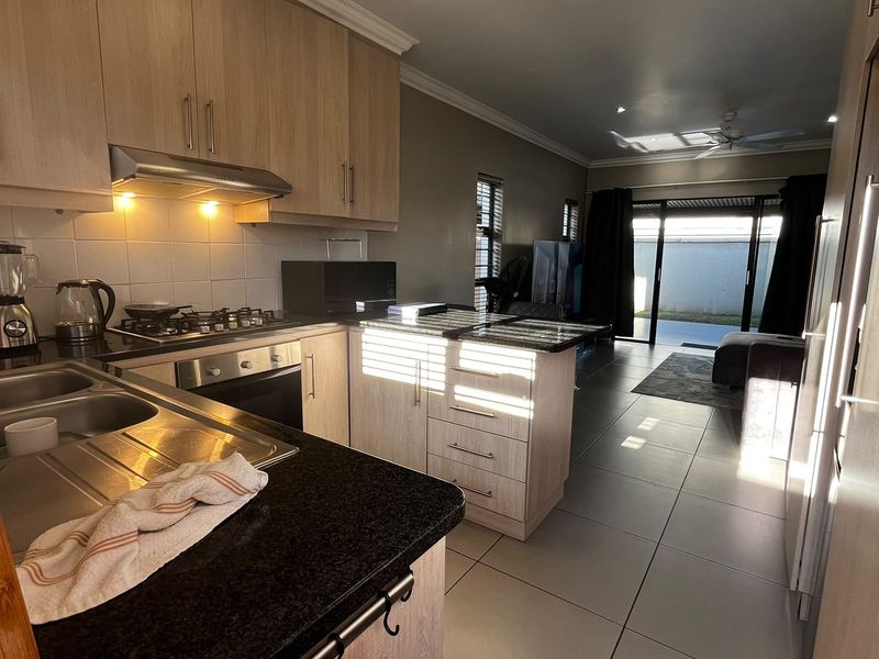 Open-plan kitchen and living area featuring light wood cabinetry, granite countertops, gas hob, and direct access to an outdoor patio through sliding glass doors.
